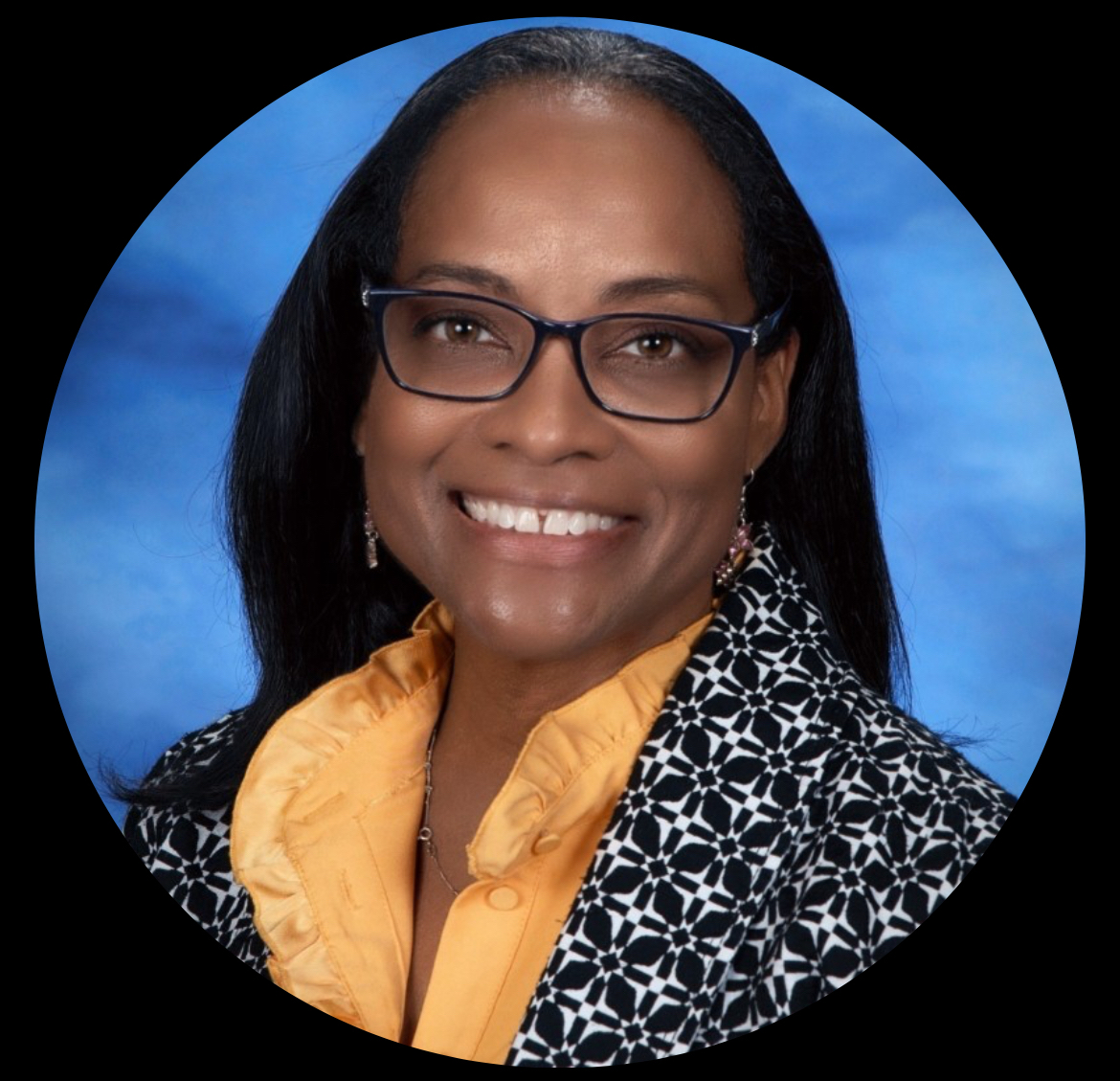 woman in yellow blouse under a patterned jacket, she is wearing glasses