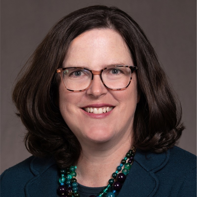 Professional woman with shoulder length brown hair, tortiseshell glasses and a green multi-strand bead necklace