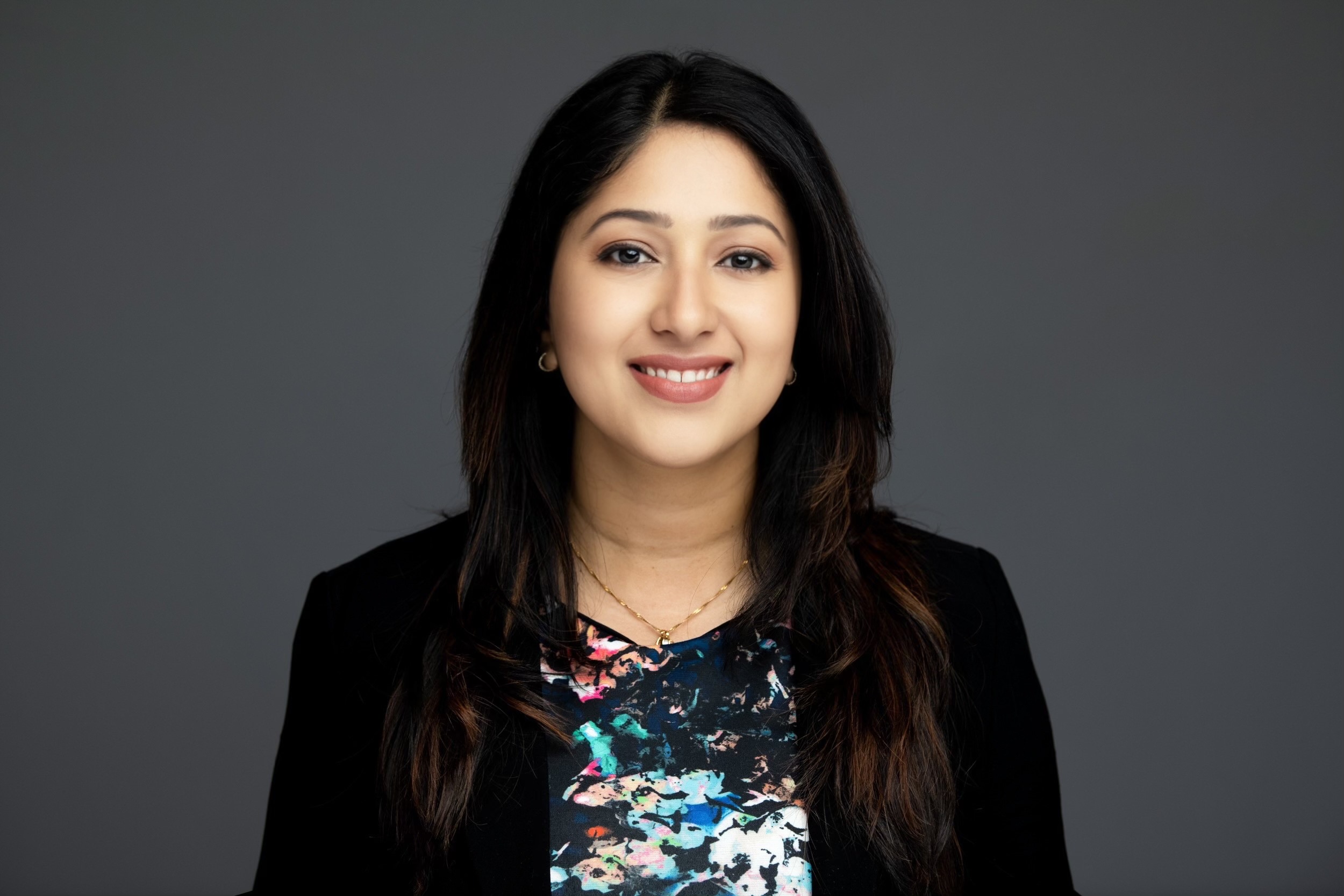 Woman with long dark hair.  She is wearing a colorful top and a black blazer.